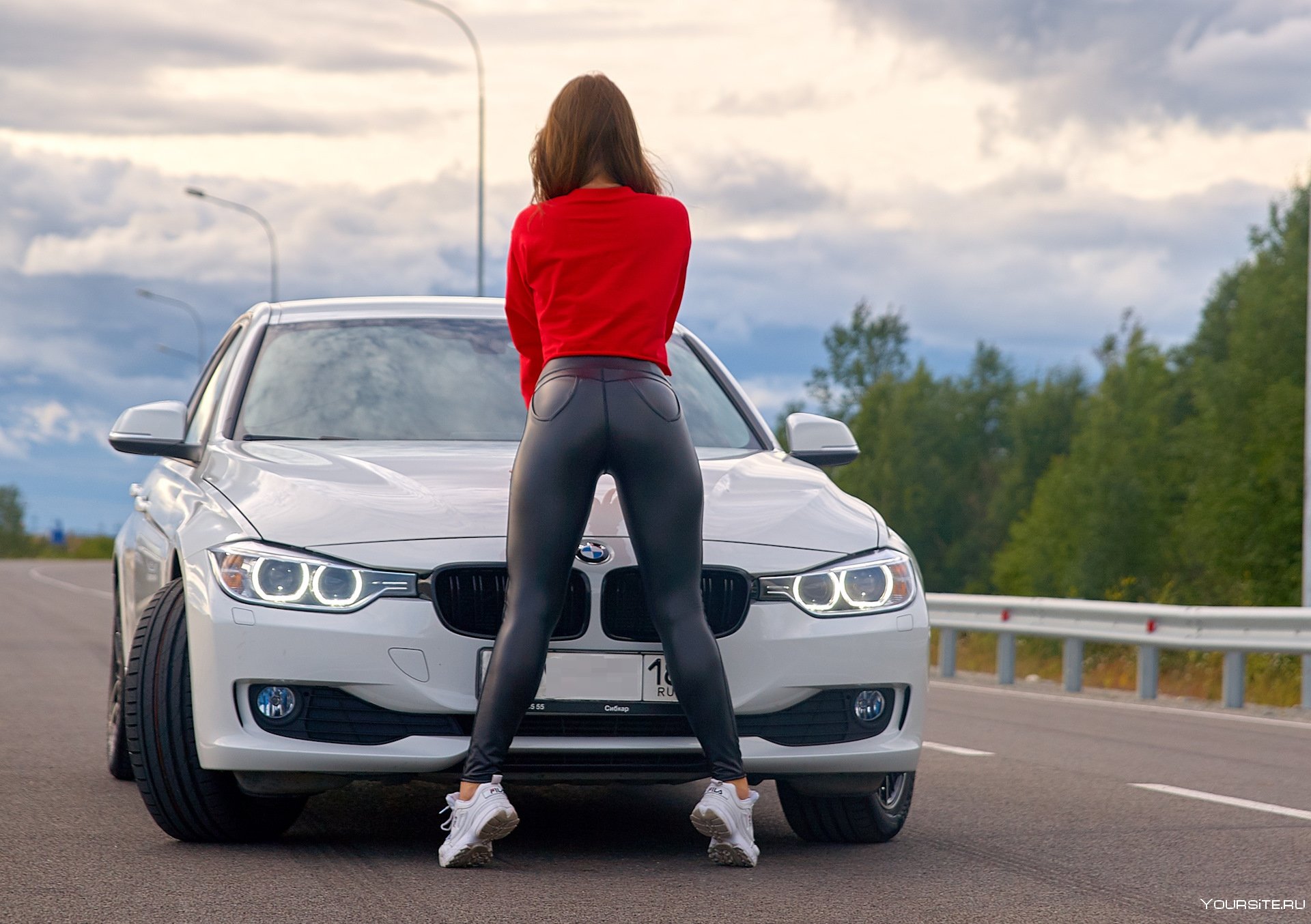 Молодая женщина показывает свою маленькую грудь облокатившись на капот спортивного авто 