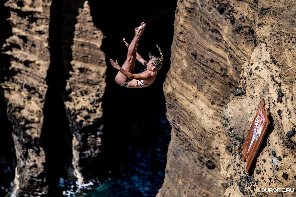 Девушка прыгает со скалы в воду