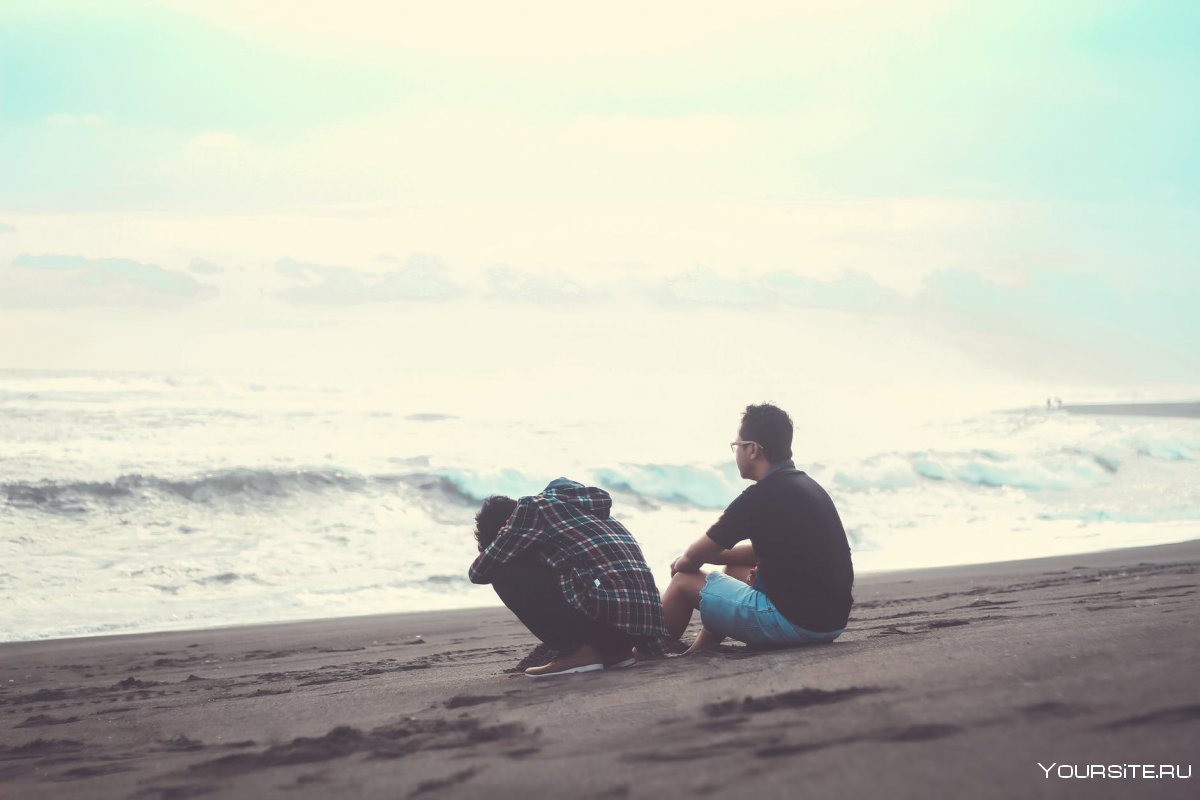 Мужчина сидит на песке у моря
